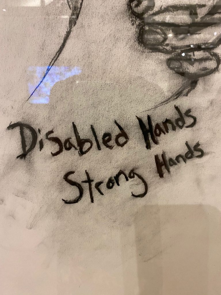Charcoal drawing with lettering "Disabled Hands, Strong Hands" with a partial image of a hand in the top right corner.